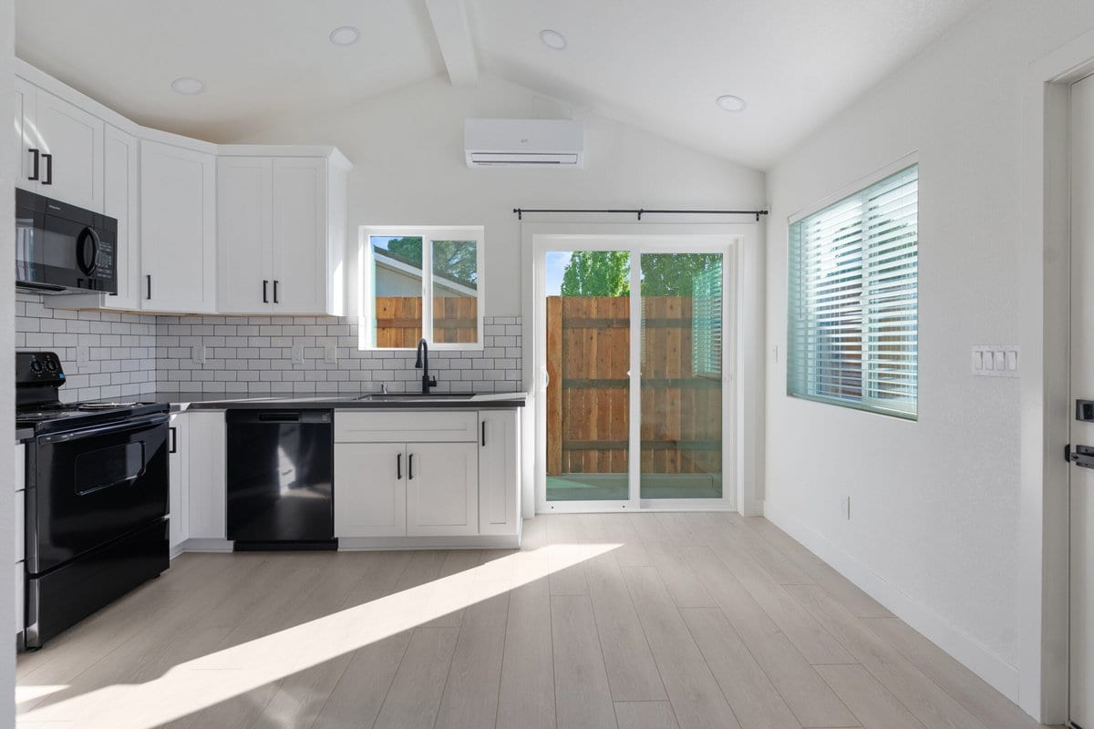 New ADU kitchen with white shaker cabinets, subway tile backsplash, dark counters and a sliding door to a fenced patio
