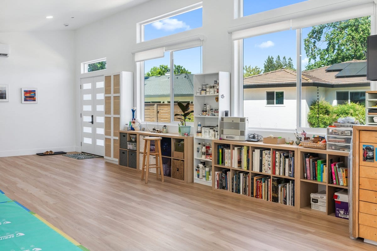 Interior of a finished studio ADU with vaulted ceiling, full-height windows, plank flooring and a mini-split head